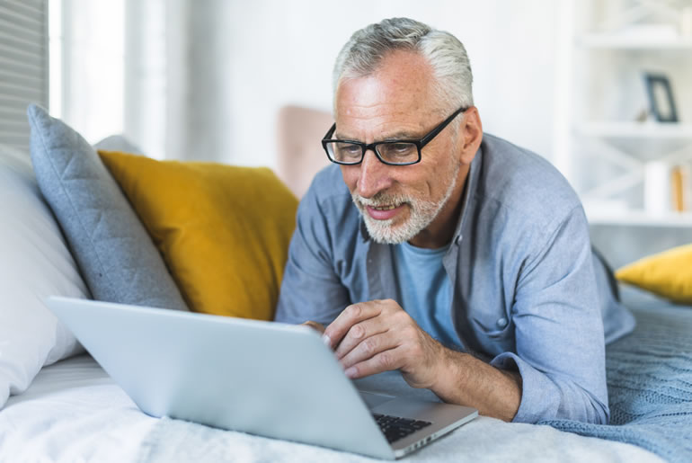 retired senior man relaxing bed looking laptop compressed
